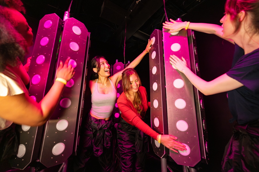 Three persons playing at the room, pressing buttons with lights.
